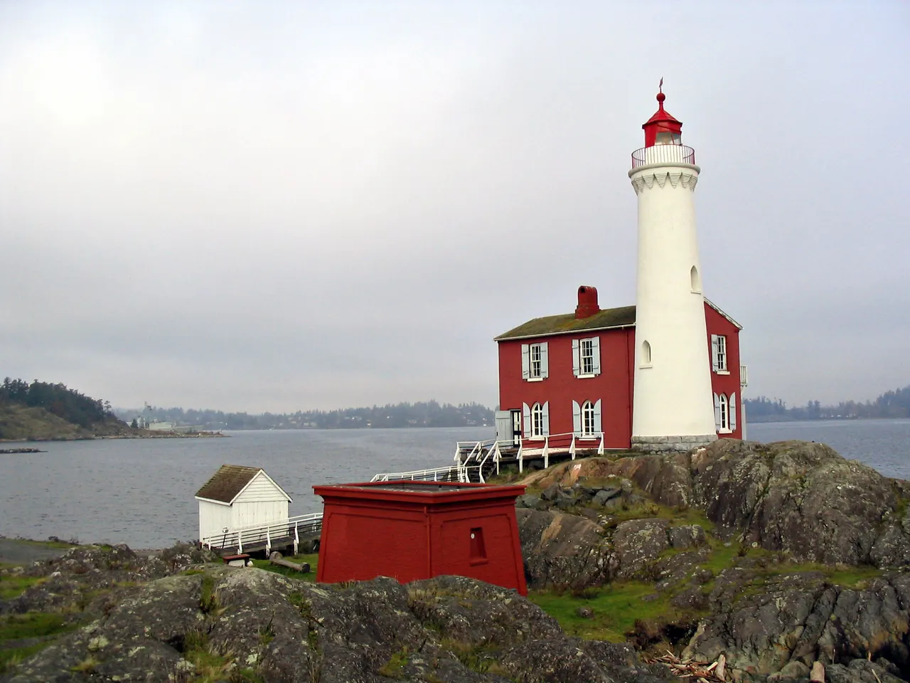 Farol de Fisgard, uma torre branca ao lado de uma casa vermelha, sobre rochas à beira-mar na região de Victoria.